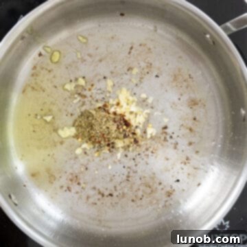Minced garlic, oregano, and crushed red pepper sautéing in olive oil in a saucepan, releasing their fragrance.
