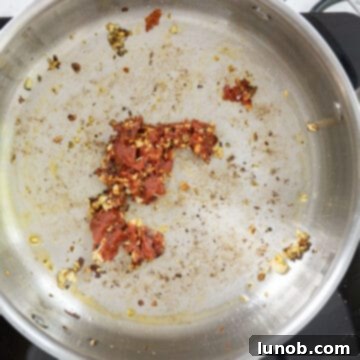 Tomato paste being stirred into the sautéed garlic and seasonings in a saucepan, beginning to caramelize.