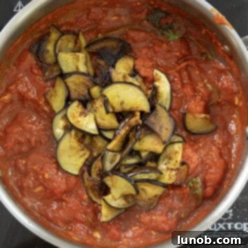 Golden fried eggplant pieces carefully added to the simmering tomato sauce in a saucepan.