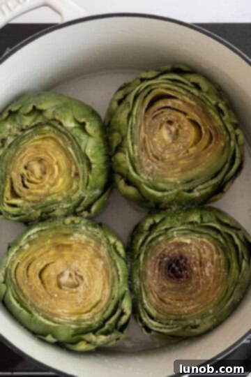 Tender Steamed Artichokes Made Simple 5 Four trimmed artichokes neatly arranged in a pot with water and oil.