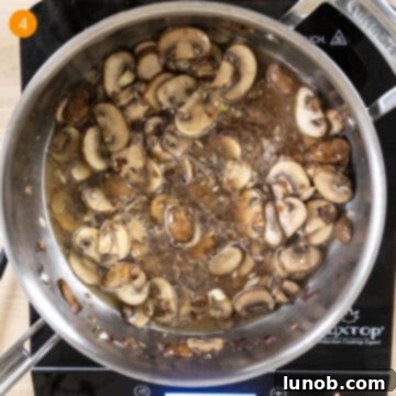 Velvety Garlic Mushroom Pasta 7 Simmering white wine with mushrooms in pan.
