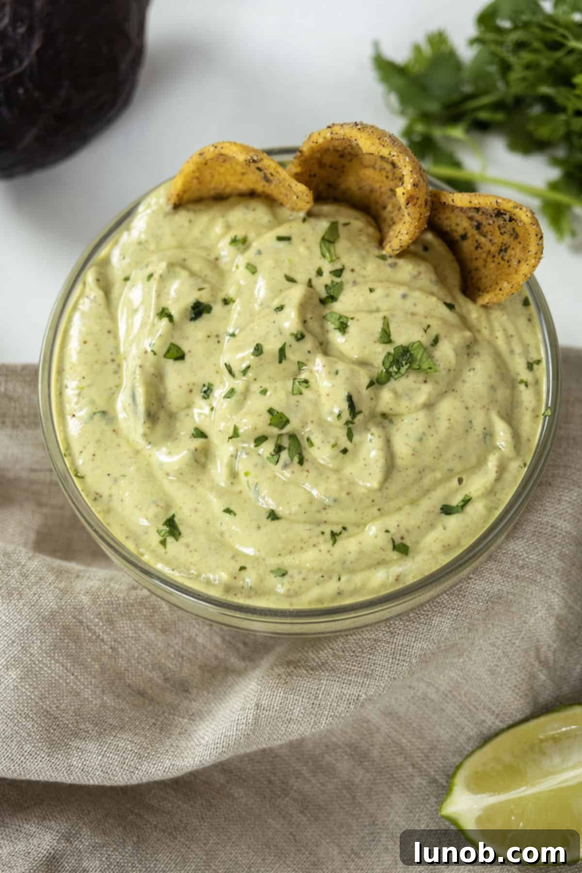 Fresh Avocado Lime Crema 10 avocado lime crema in a glass bowl with limes and cilantro on side and chips in the crema.