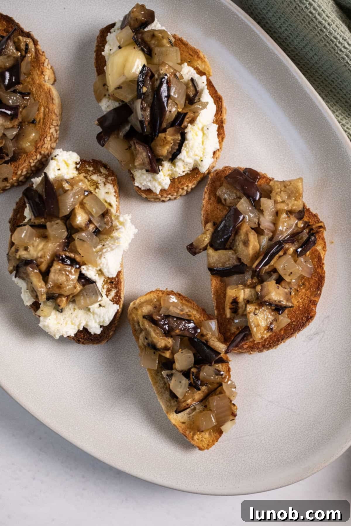 Tangy Marinated Eggplant and Onion 2 Marinated eggplant and onion on crispy toast with creamy ricotta cheese, garnished with fresh herbs.