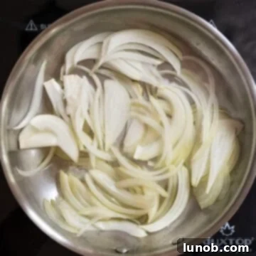 Sliced onions sizzling in olive oil within a hot cast iron frying pan, starting the caramelization process.