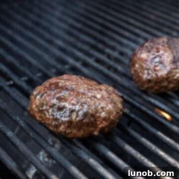 Burger patties searing on a hot grill, showing grill marks developing.