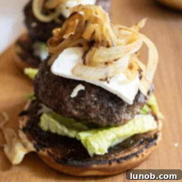 A fully assembled gourmet burger on a bun with fig jam and lettuce, topped with a goat cheese patty and caramelized onions.