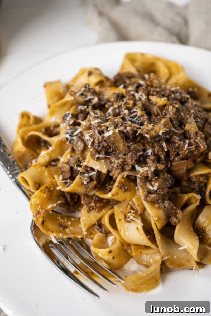 Lamb ragu over pappardelle on a small plate, garnished with fresh herbs and Pecorino Romano.