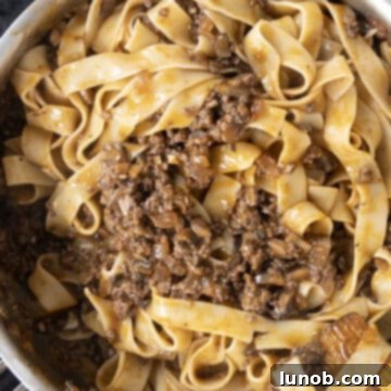 Pappardelle pasta being stirred into the lamb ragu in a saucepan, ensuring every strand is coated.