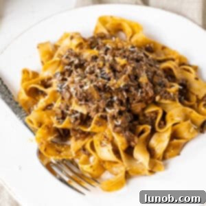 Lamb ragu over pappardelle on a small plate, garnished with fresh herbs.