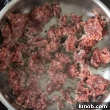 Ground lamb searing undisturbed in a large saucepan, developing a rich brown crust.