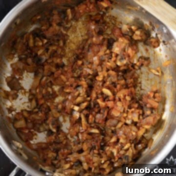 Tomato paste stirred into sautéed vegetables in a saucepan, caramelizing on the bottom.