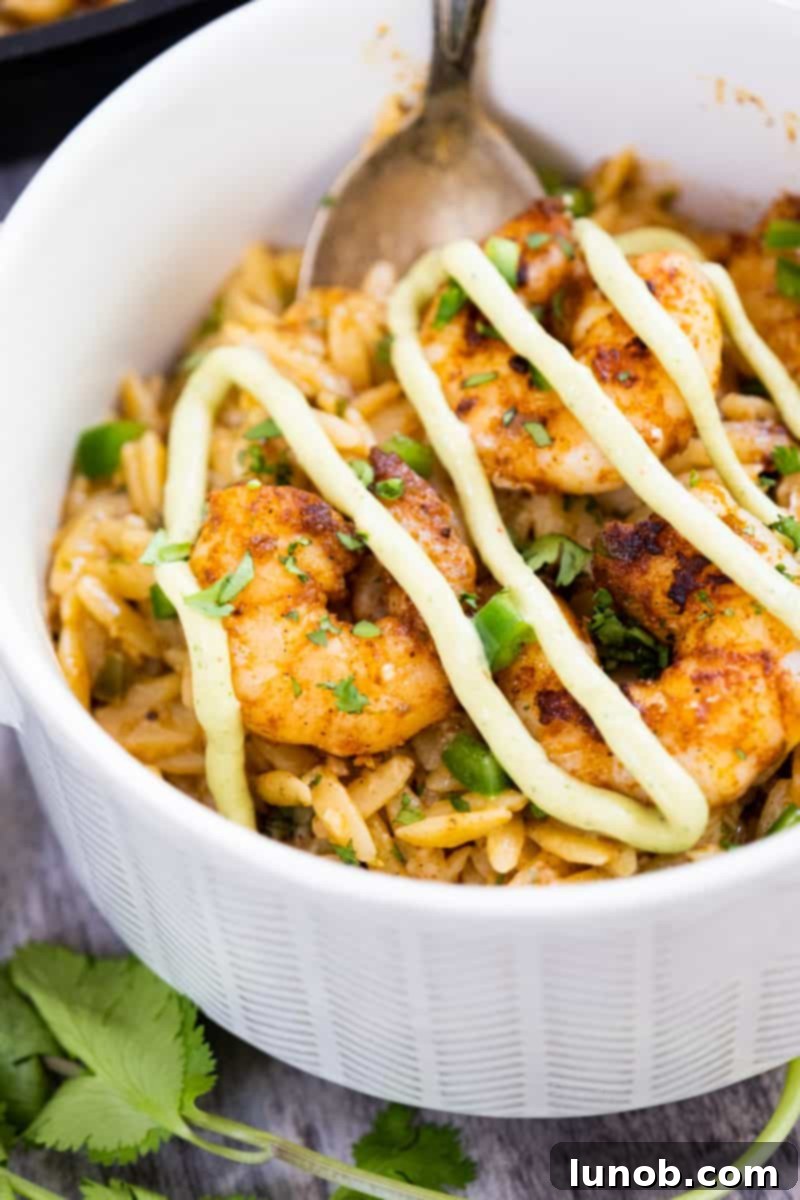 close-up of spicy cast iron shrimp topped with avocado crema over creamy cilantro lime orzo, garnished with fresh cilantro