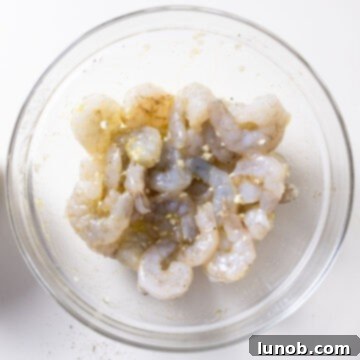 Silken Pesto Shrimp Delight 5 Raw shrimp marinating with minced garlic and olive oil in a ceramic bowl.