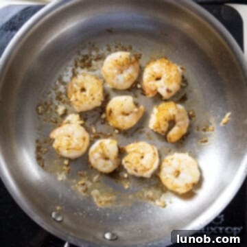 Silken Pesto Shrimp Delight 6 Plump shrimp searing in a hot stainless steel pan, turning pink and opaque.