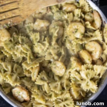 Silken Pesto Shrimp Delight 8 Vibrant green pesto being stirred into pasta and shrimp in a pan, creating a creamy sauce.