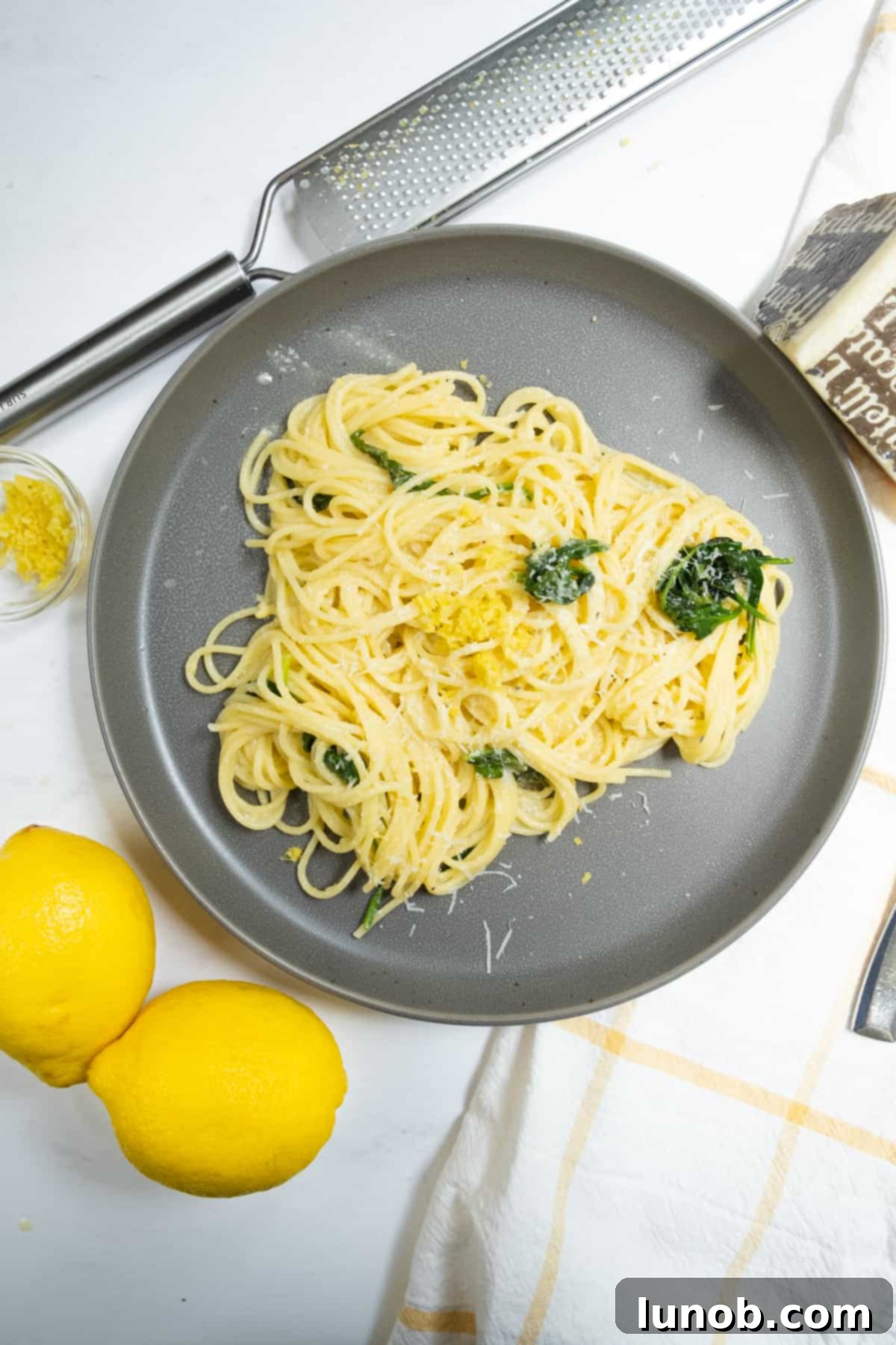 A beautifully plated lemon spinach pasta dish, garnished with fresh lemon slices, zest, and a sprinkle of Pecorino Romano cheese on the side, highlighting its vibrant and fresh ingredients.