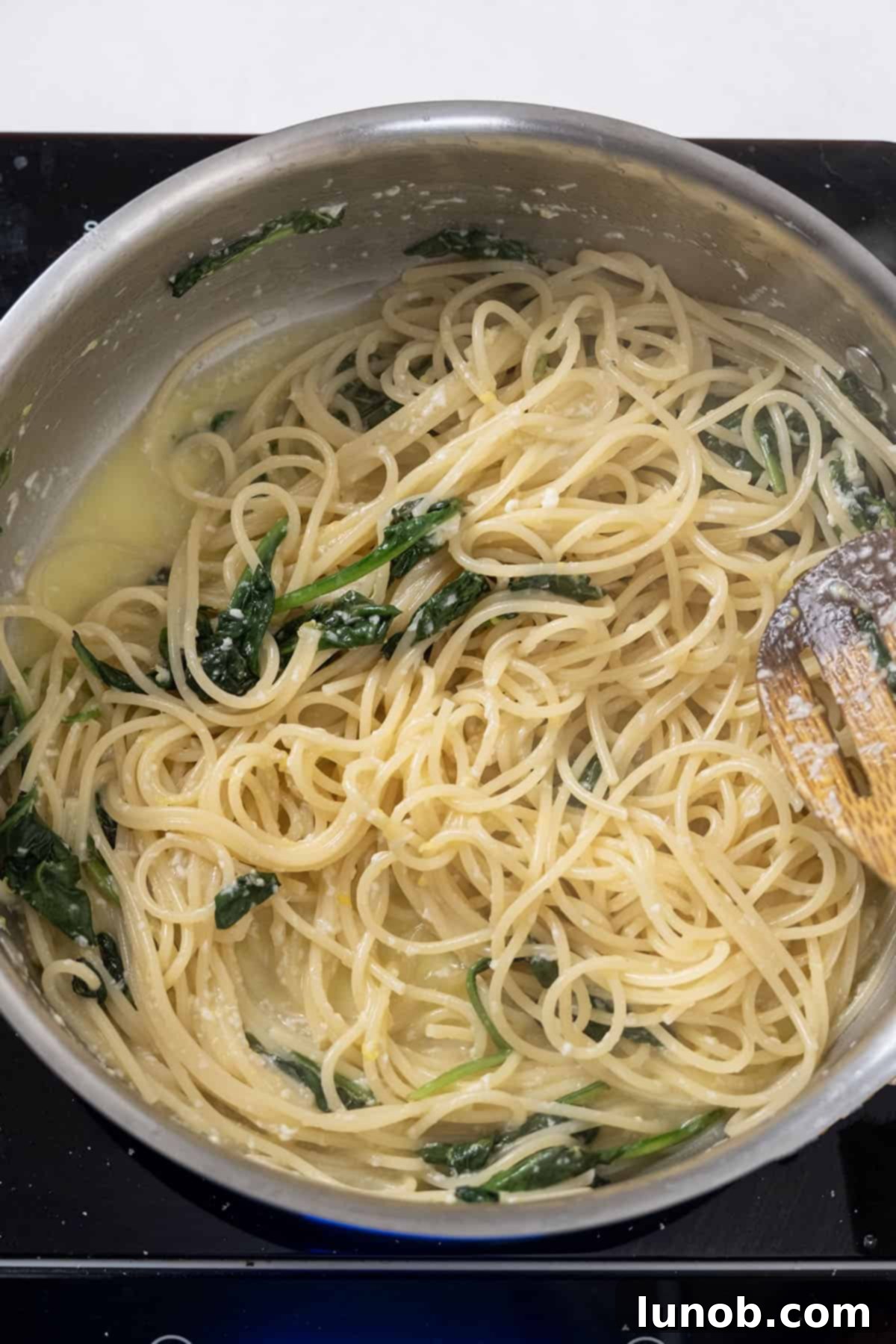 The lemon-Pecorino Romano mixture being poured over the spaghetti and spinach in a large saucepan, creating a creamy sauce.