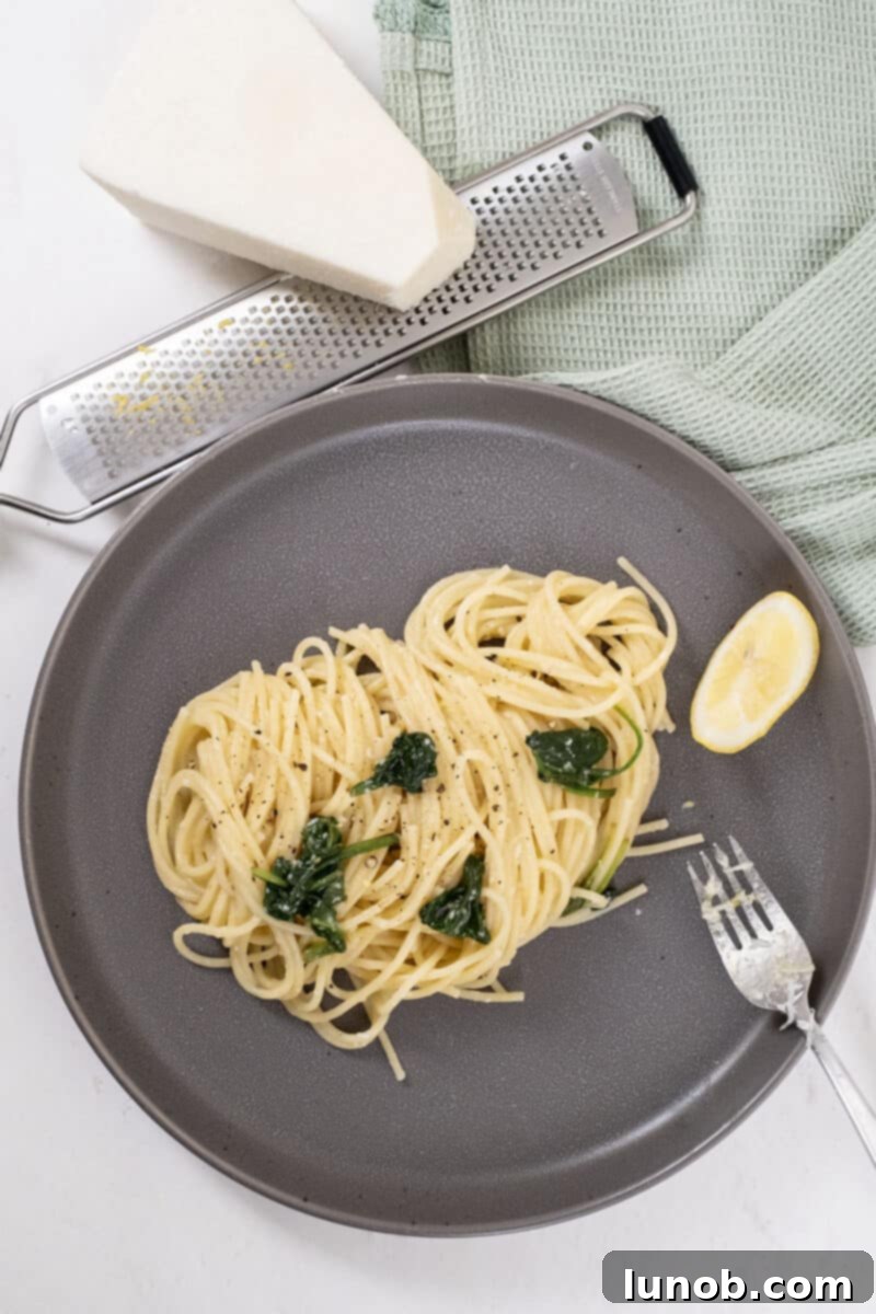 A serving of creamy lemon spinach pasta in a bowl, garnished with fresh lemon zest and a sprinkle of Pecorino Romano, ready to be enjoyed.