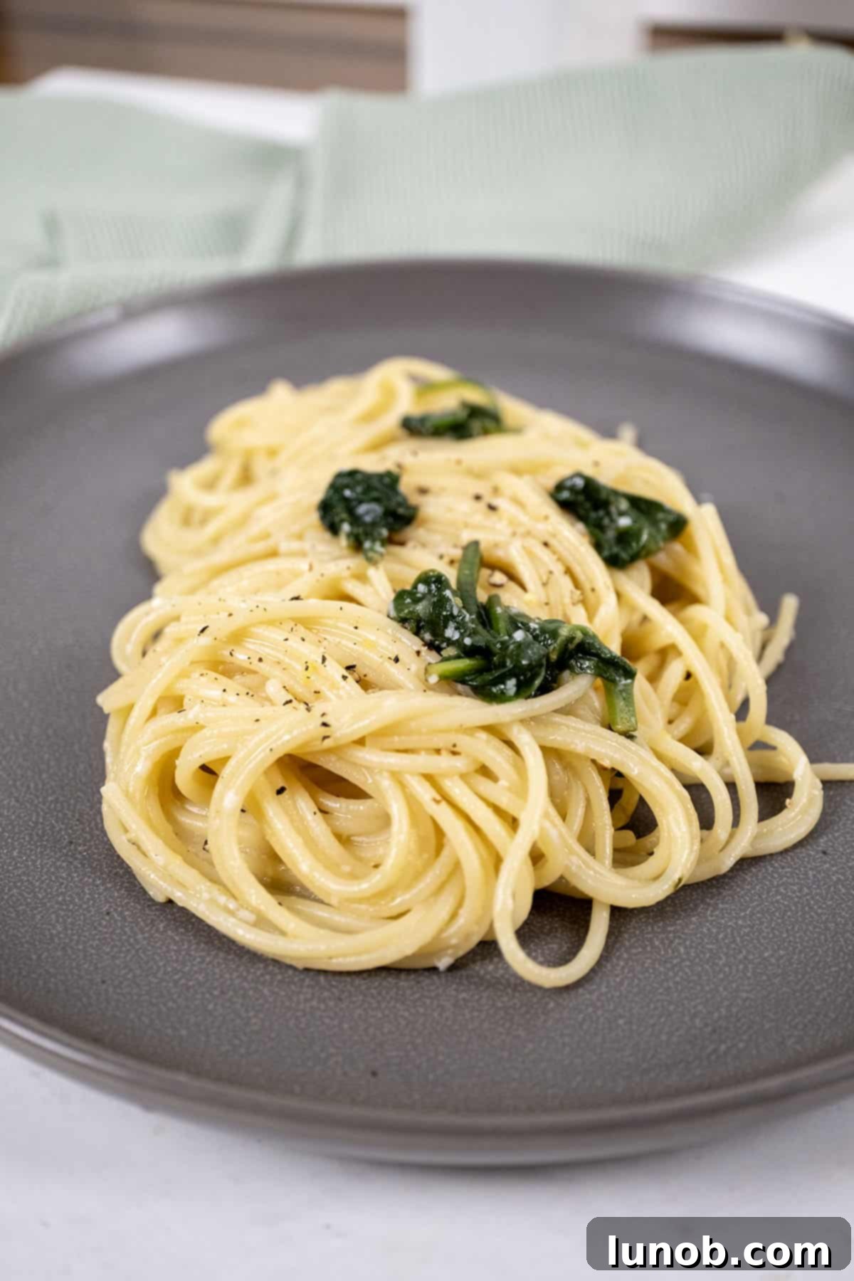 Close-up shot of creamy lemon spinach pasta in a large pan, showcasing the vibrant green spinach, yellow lemon zest, and rich sauce coating the spaghetti.