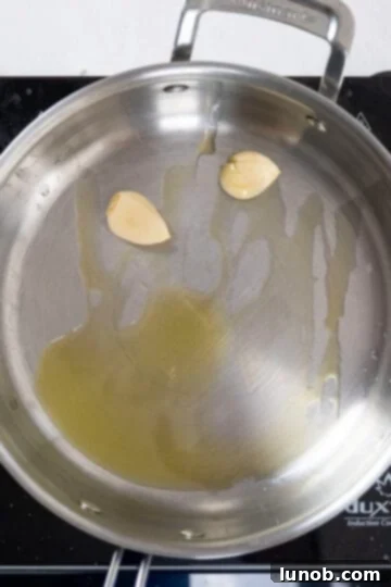 Two crushed garlic cloves sizzling in olive oil in a hot saucepan, browning gently to infuse the oil with flavor.