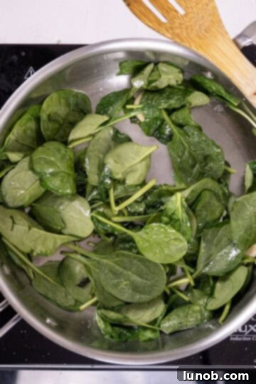 Fresh spinach wilting in a hot saucepan with infused garlic oil, beginning to reduce in volume.