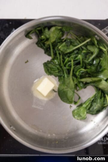 A knob of butter melting in an empty section of a saucepan, away from the wilted spinach, preventing the spinach from absorbing all the butter.