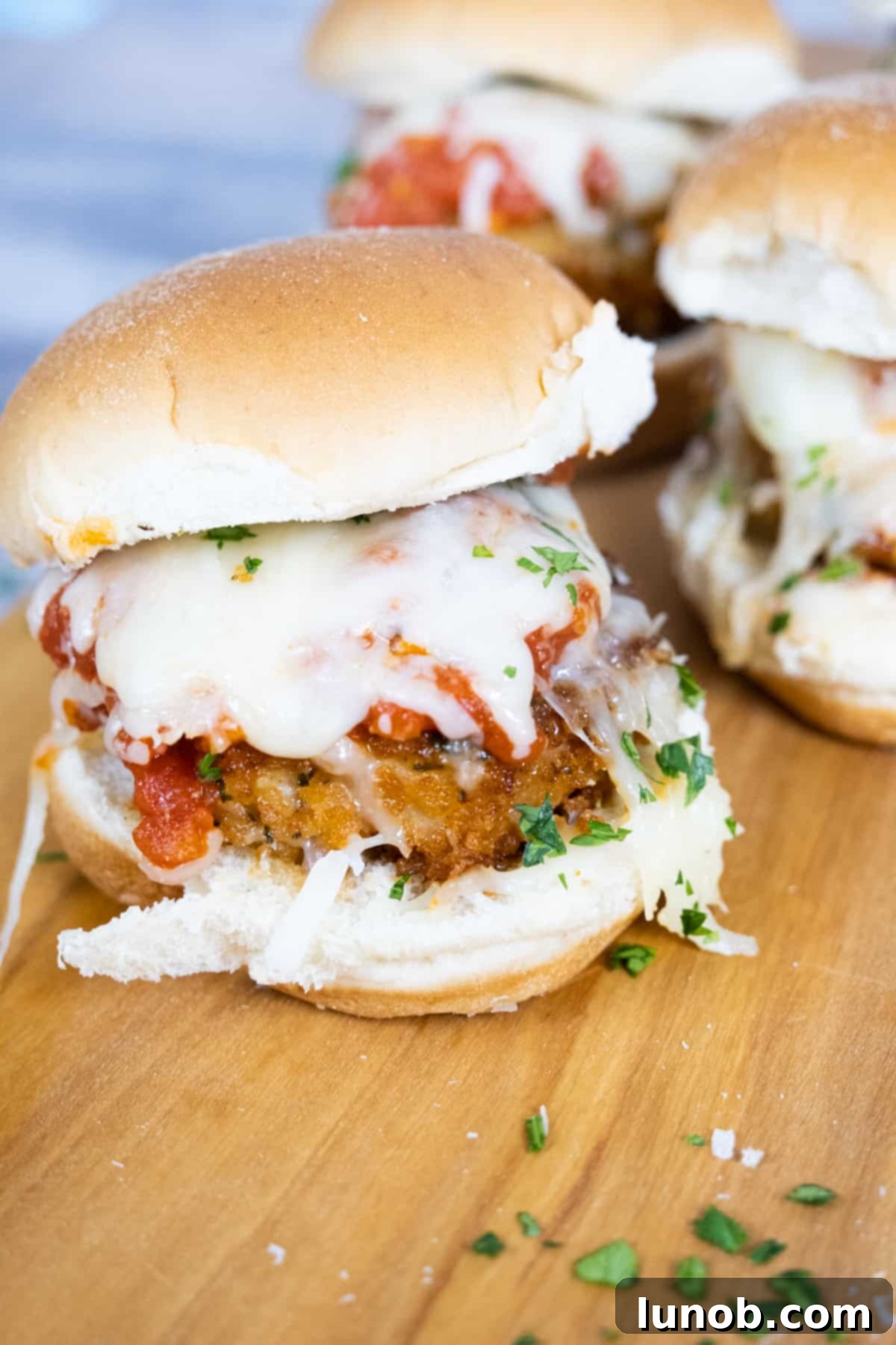 Crispy chicken parm sliders generously topped with rich tomato sauce and bubbling melted mozzarella cheese, garnished with fresh parsley.