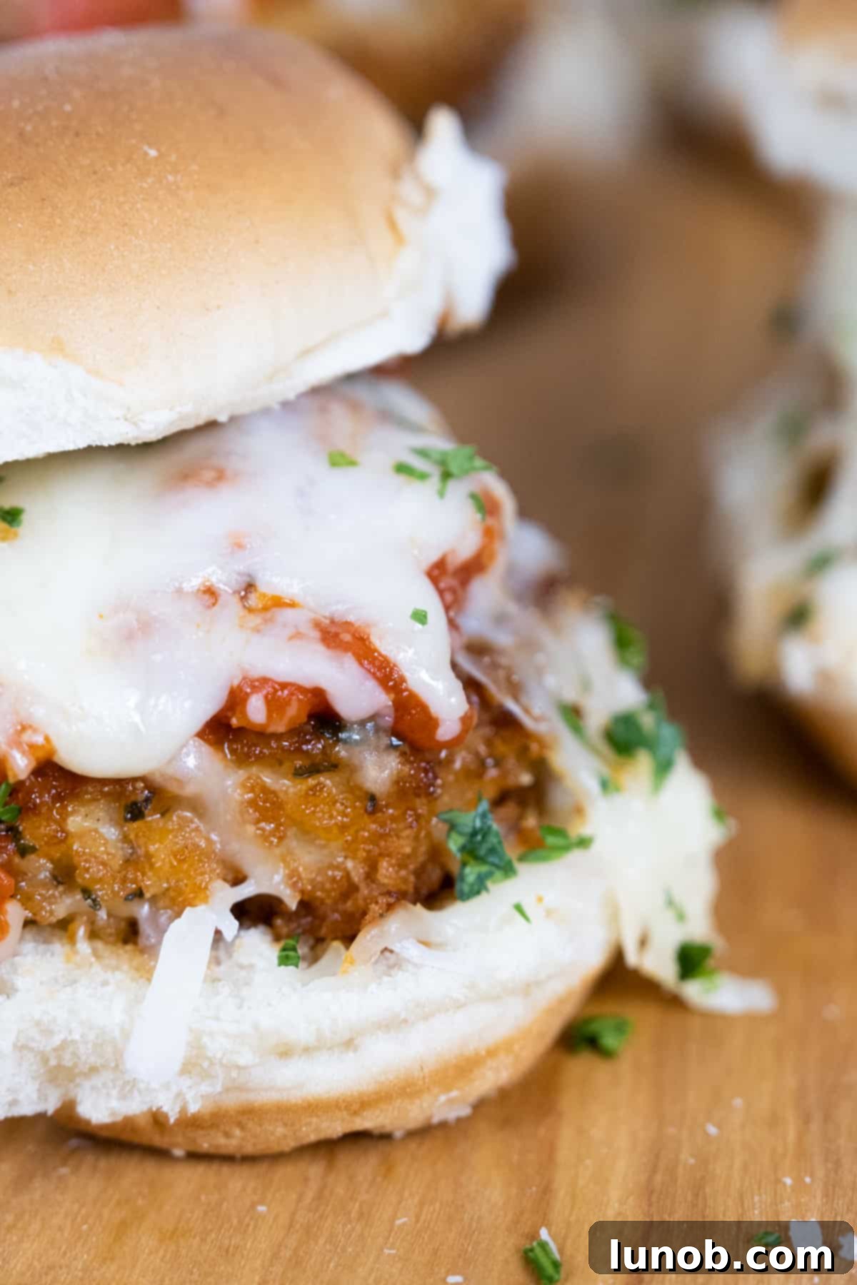 Close-up of a golden-brown chicken parm slider, showcasing melted mozzarella and rich tomato sauce, ready to be enjoyed.