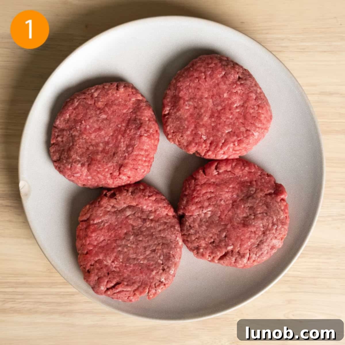 Bacon Blue Cheese Burger 4 Four perfectly formed burger patties seasoned with salt and pepper, ready for grilling, presented on a white plate.