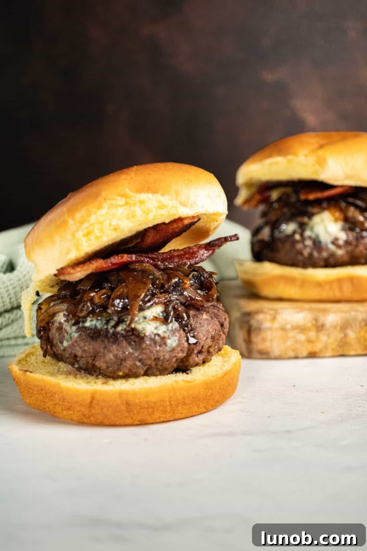 Bacon Blue Cheese Burger 10 A fully assembled Bacon Blue Cheese Burger on a cutting board, garnished with crispy bacon and a generous dollop of onion jam, ready to be served.