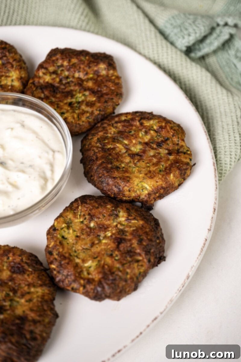 Crispy Air-Fried Zucchini Fritters 2 A plate of golden-brown zucchini fritters with a bowl of creamy dip and fresh herbs.