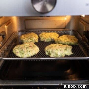 Crispy Air-Fried Zucchini Fritters 10 Zucchini fritters cooking inside an air fryer basket, turning golden brown.