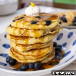 Lemon ricotta blueberry pancakes covered with syrup with a dollop of ricotta on top.