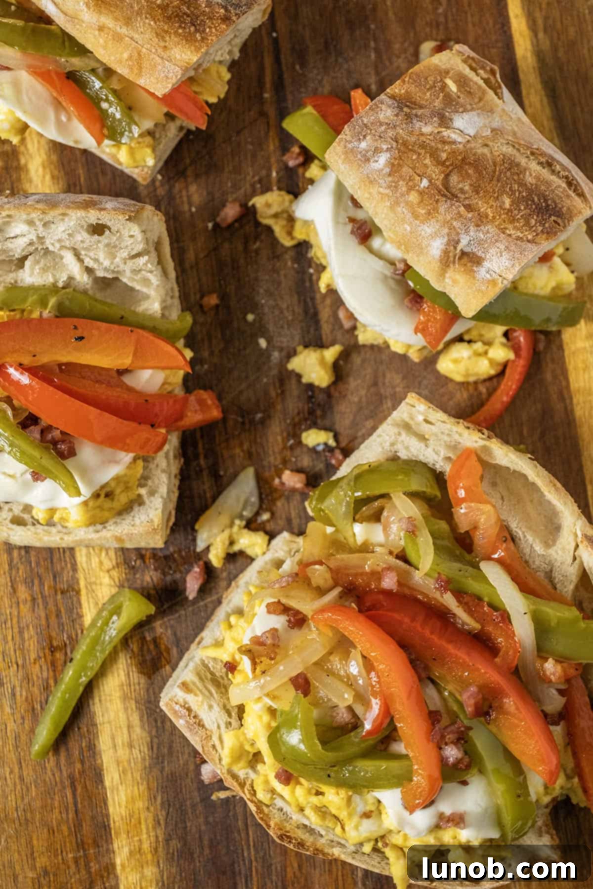 Classic Pepper & Egg Sub 10 3 Peppers and eggs sandwiches with mozzarella and pancetta on Italian Bread on a cutting board.