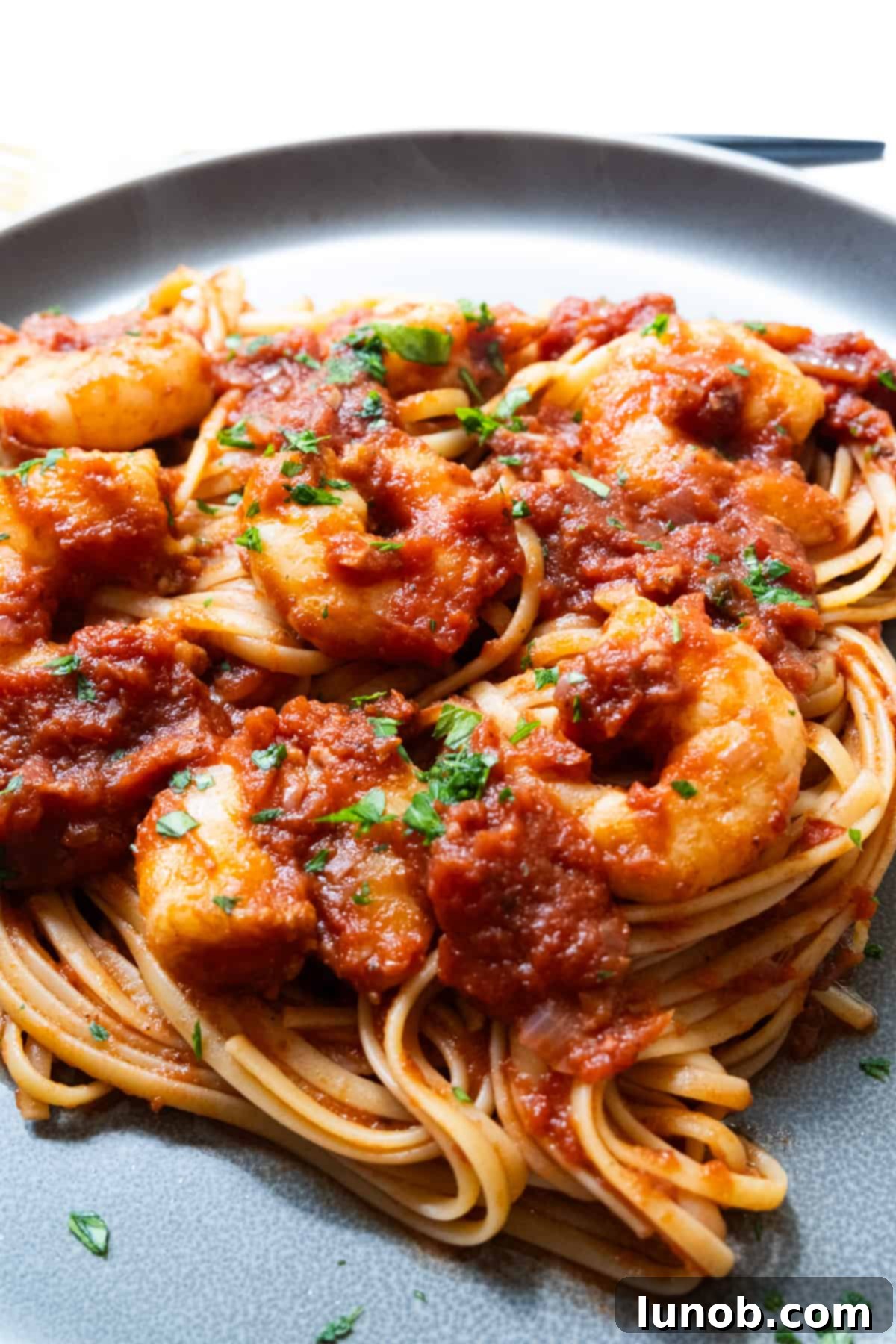 Fiery Fra Diavolo Shrimp Linguine 11 A generous serving of Shrimp Fra Diavolo with linguine on a white plate, garnished with fresh herbs and a lemon wedge.