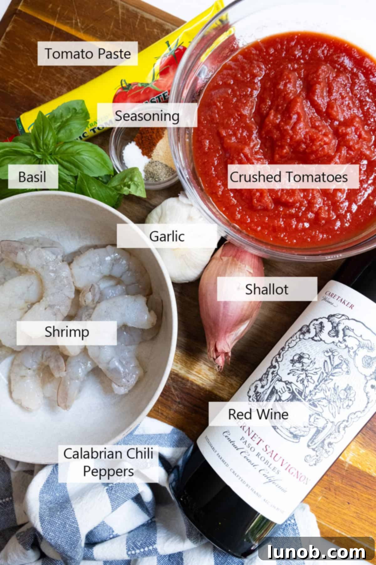 Fiery Fra Diavolo Shrimp Linguine 3 A selection of fresh ingredients including raw shrimp, linguine, tomatoes, garlic, shallots, basil, red wine, and Calabrian chili peppers on a wooden board.