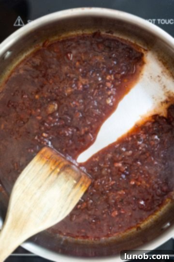 Fiery Fra Diavolo Shrimp Linguine 8 Red wine reduction in a saucepan, with a spoon dragged through to show its thickened consistency and rich color.