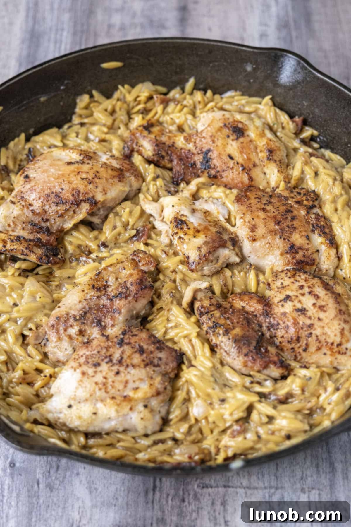 Close-up of creamy chicken bacon ranch orzo skillet with melted cheese and fresh dill.