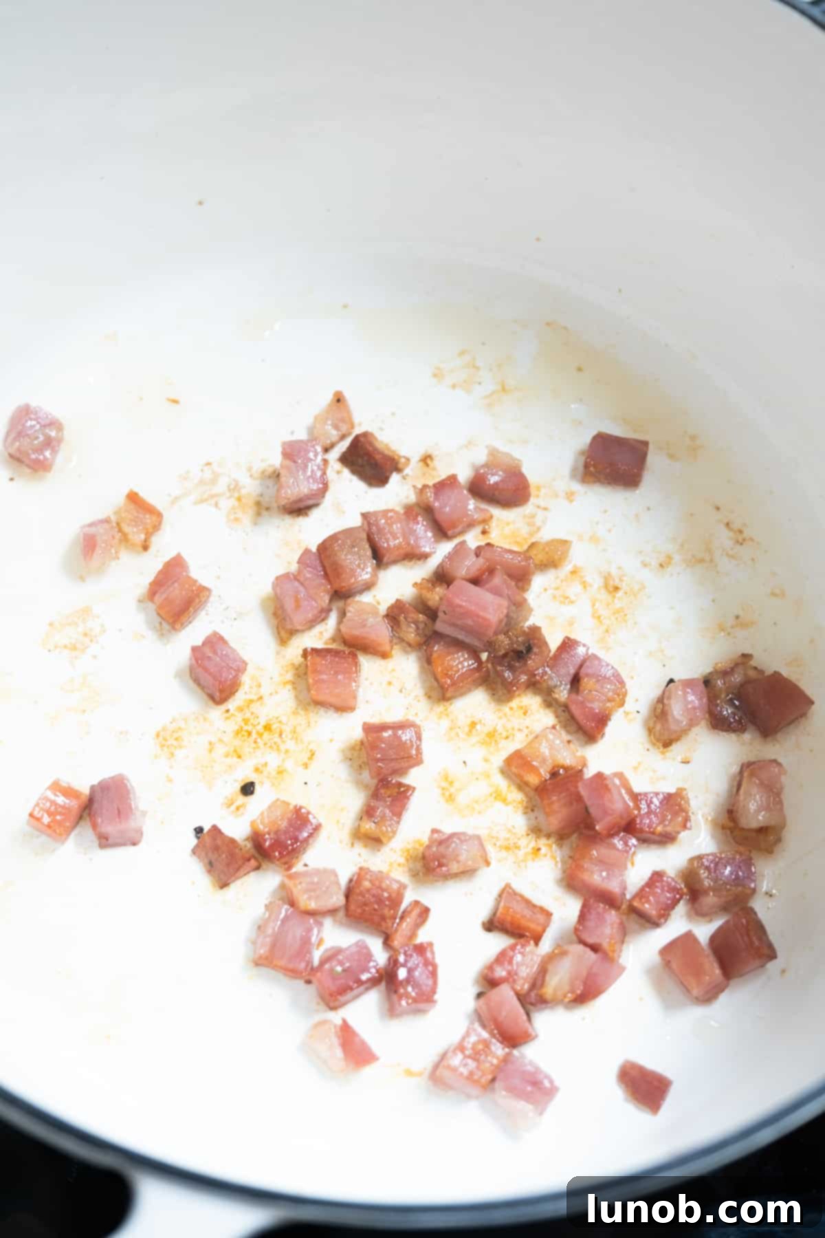 Pancetta frying in a Dutch oven, becoming golden brown and crispy