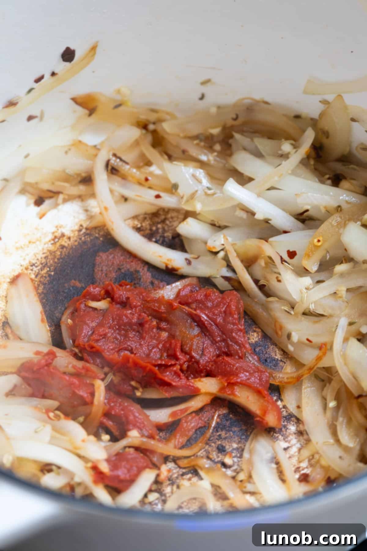Tomato paste added directly to the hot pan alongside softened onions, beginning to caramelize