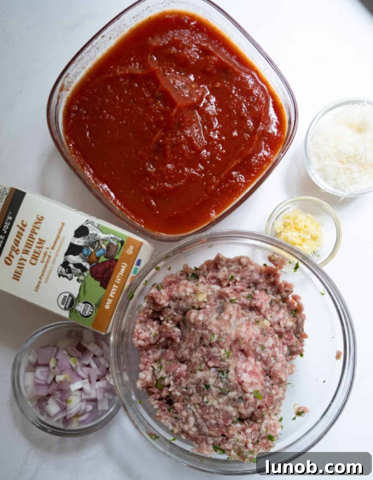 Fresh ingredients for creamy Italian pink sauce with sausage, including tomatoes, cream, sausage, and aromatics.