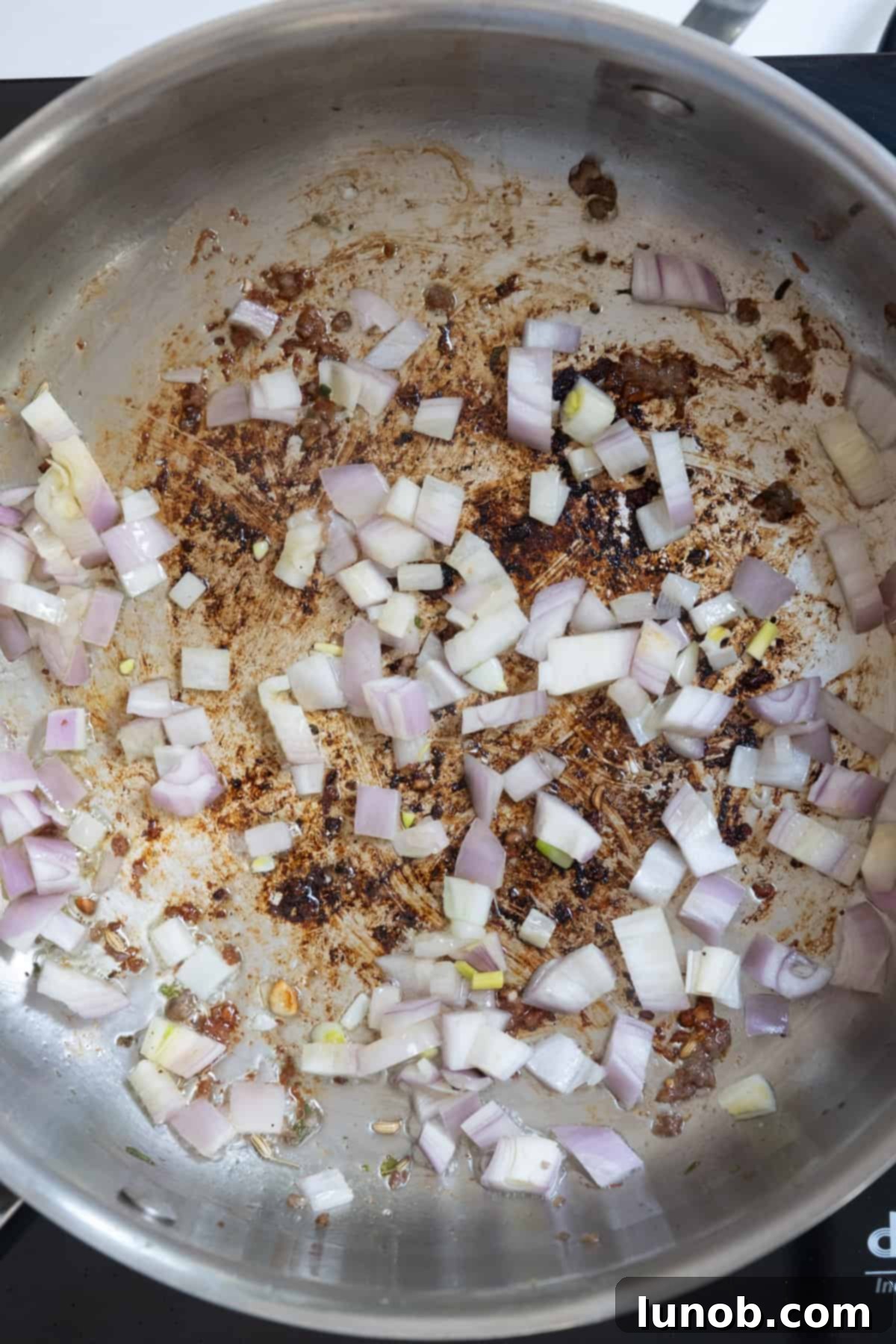 Chopped shallots gently sauteing in the pan with sausage drippings.