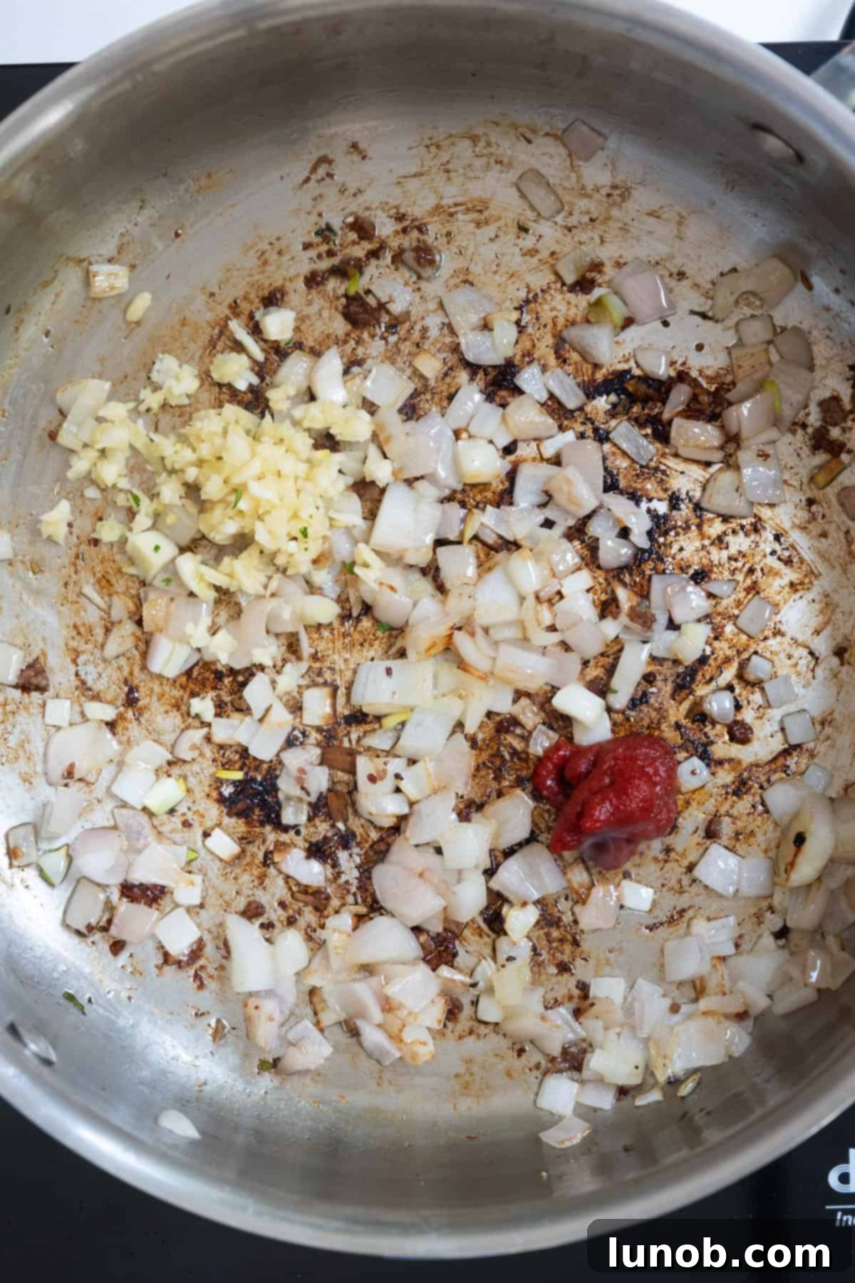 Minced garlic and tomato paste added to the softened shallots in the pan.