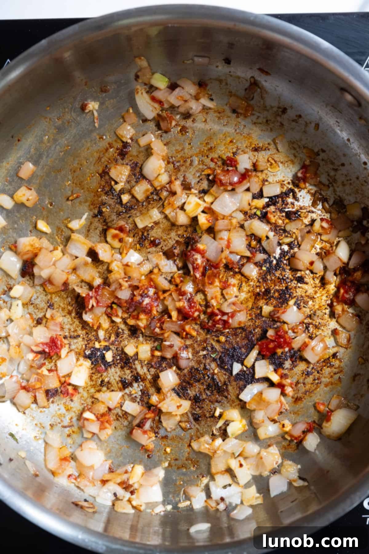 Tomato paste fully combined with shallots and garlic, caramelizing in the pan.