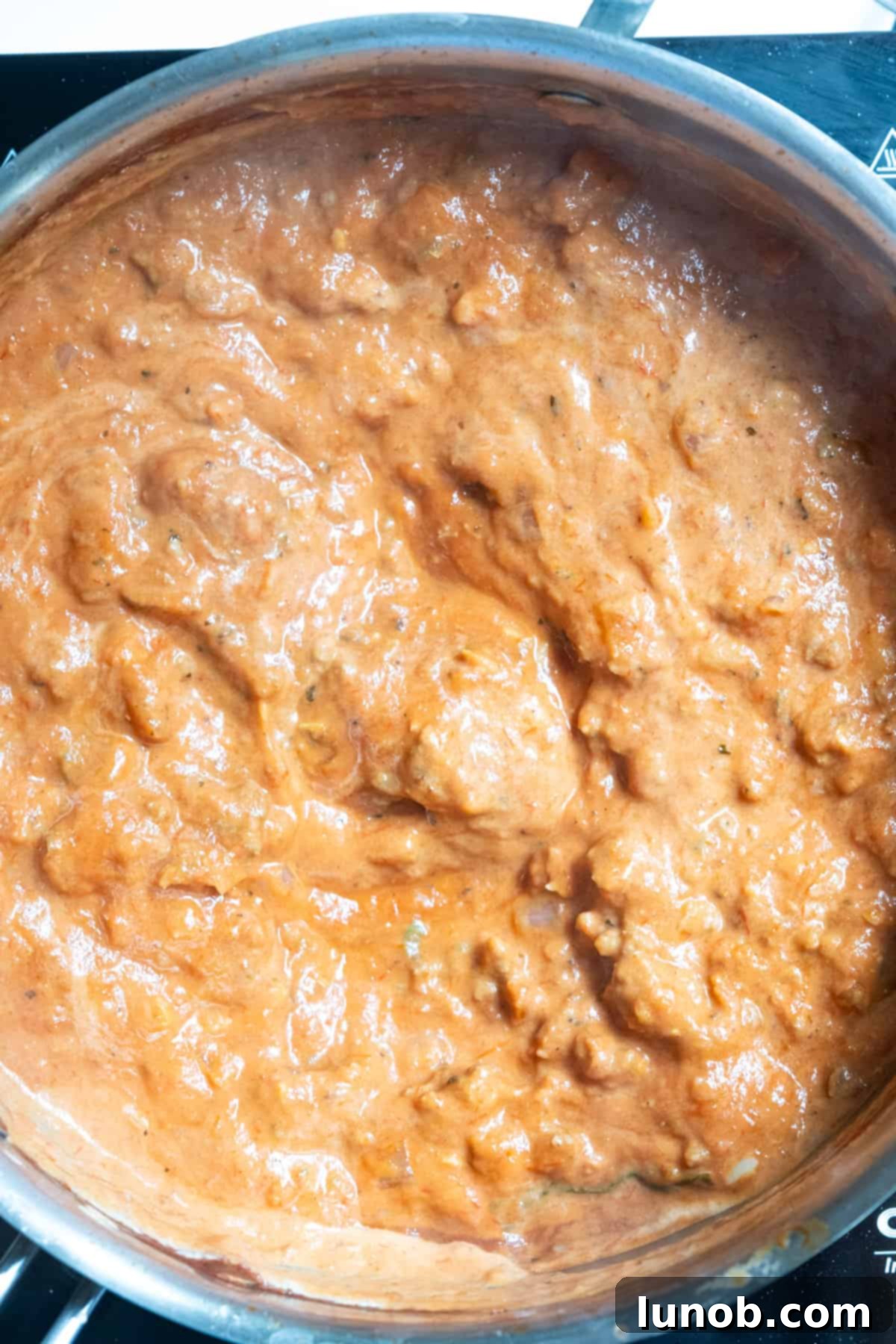 Heavy cream being stirred into the tomato sauce, transforming it into a vibrant pink sauce.