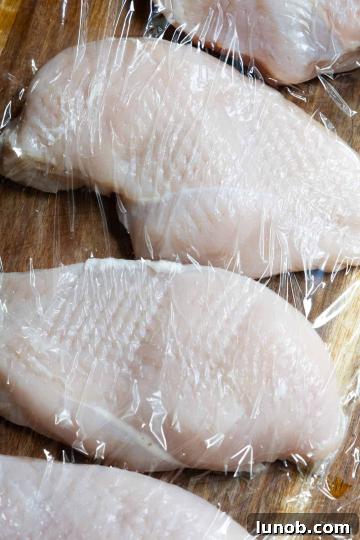 The Ultimate Cast Iron Chicken Breast 4 Tenderizing the raw chicken breast with a meat mallet between two sheets of parchment paper.