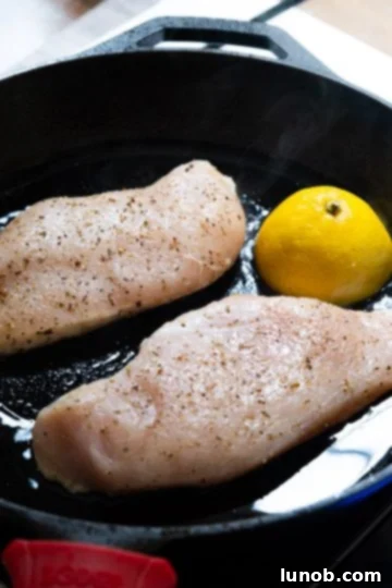 The Ultimate Cast Iron Chicken Breast 5 Raw chicken breast with half a lemon placed cut side down in a hot cast iron skillet, ready to sear.