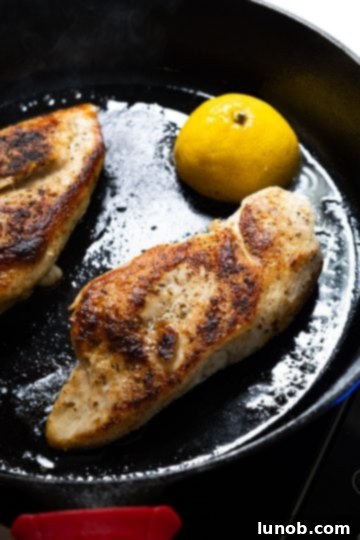 The Ultimate Cast Iron Chicken Breast 6 Chicken breast flipped over in cast iron skillet, showing a golden-brown sear, with a caramelized lemon half beside it.