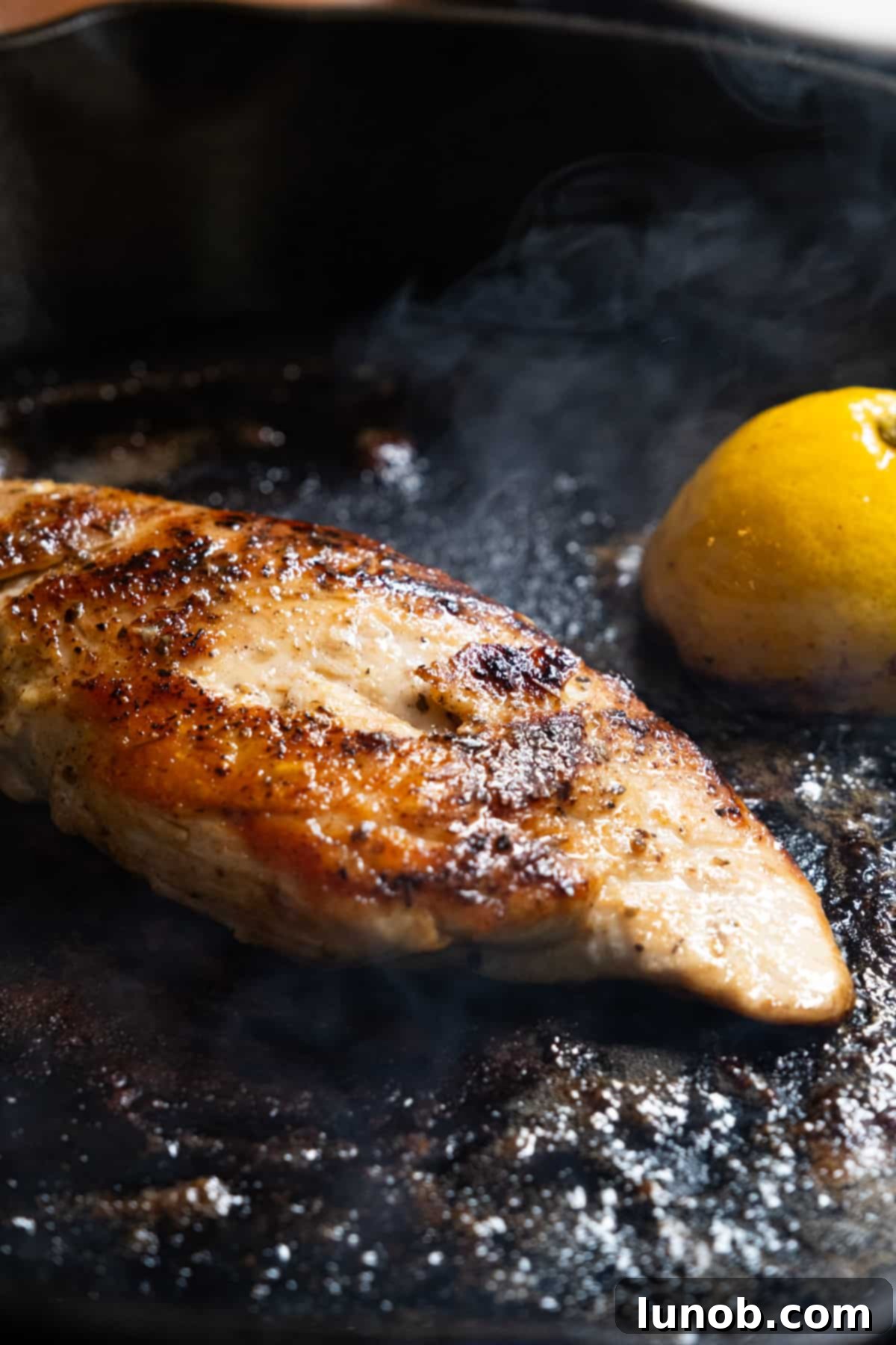 The Ultimate Cast Iron Chicken Breast 7 Chef basting a cooked cast iron chicken breast with melted butter and lemon juice in the skillet.