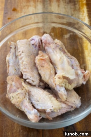 Crispy Air Fryer Garlic Parmesan Wings 4 Seasoning raw chicken wings in a mixing bowl with spices